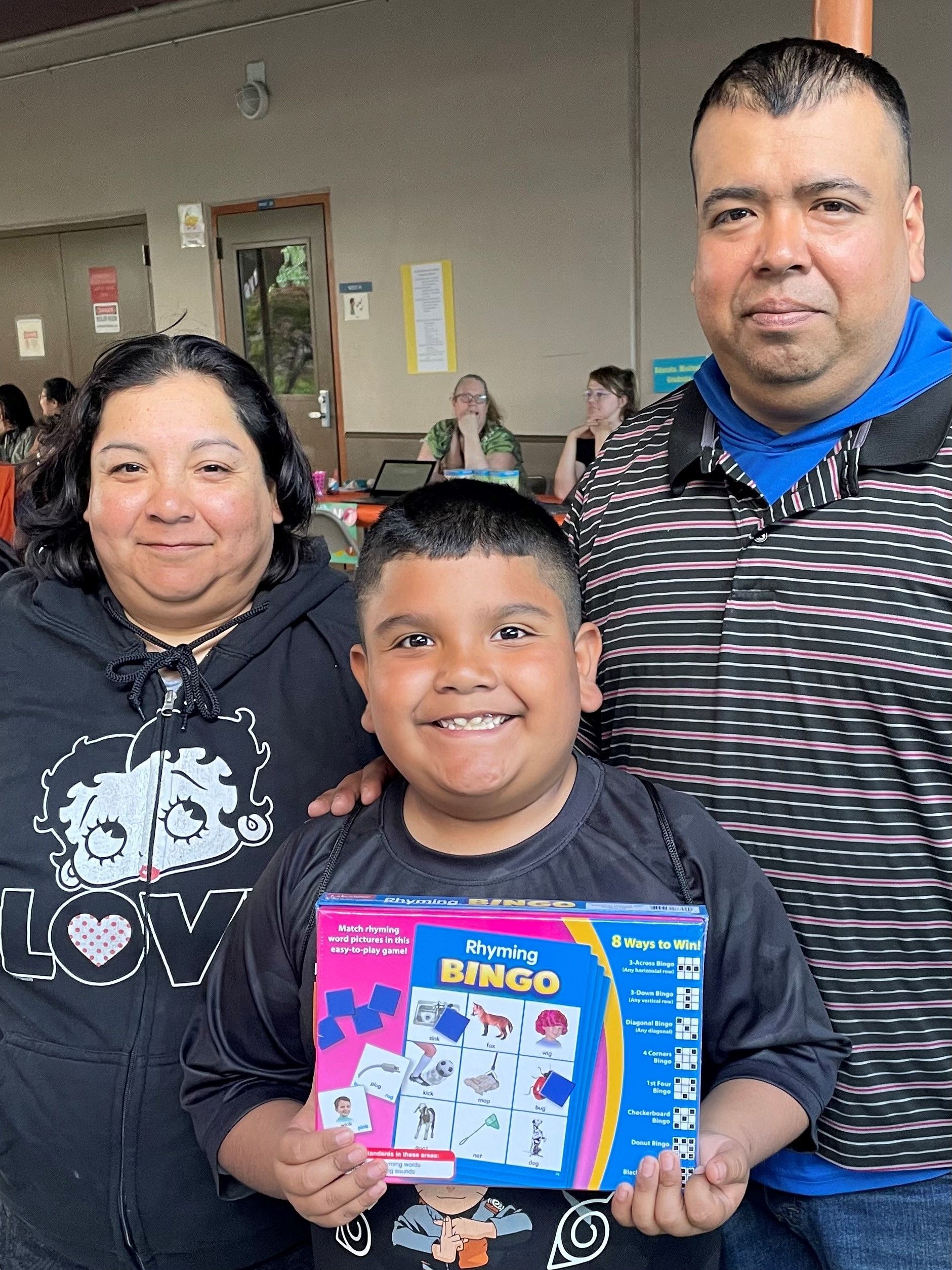A man and woman are standing next to a boy holding a bingo game.