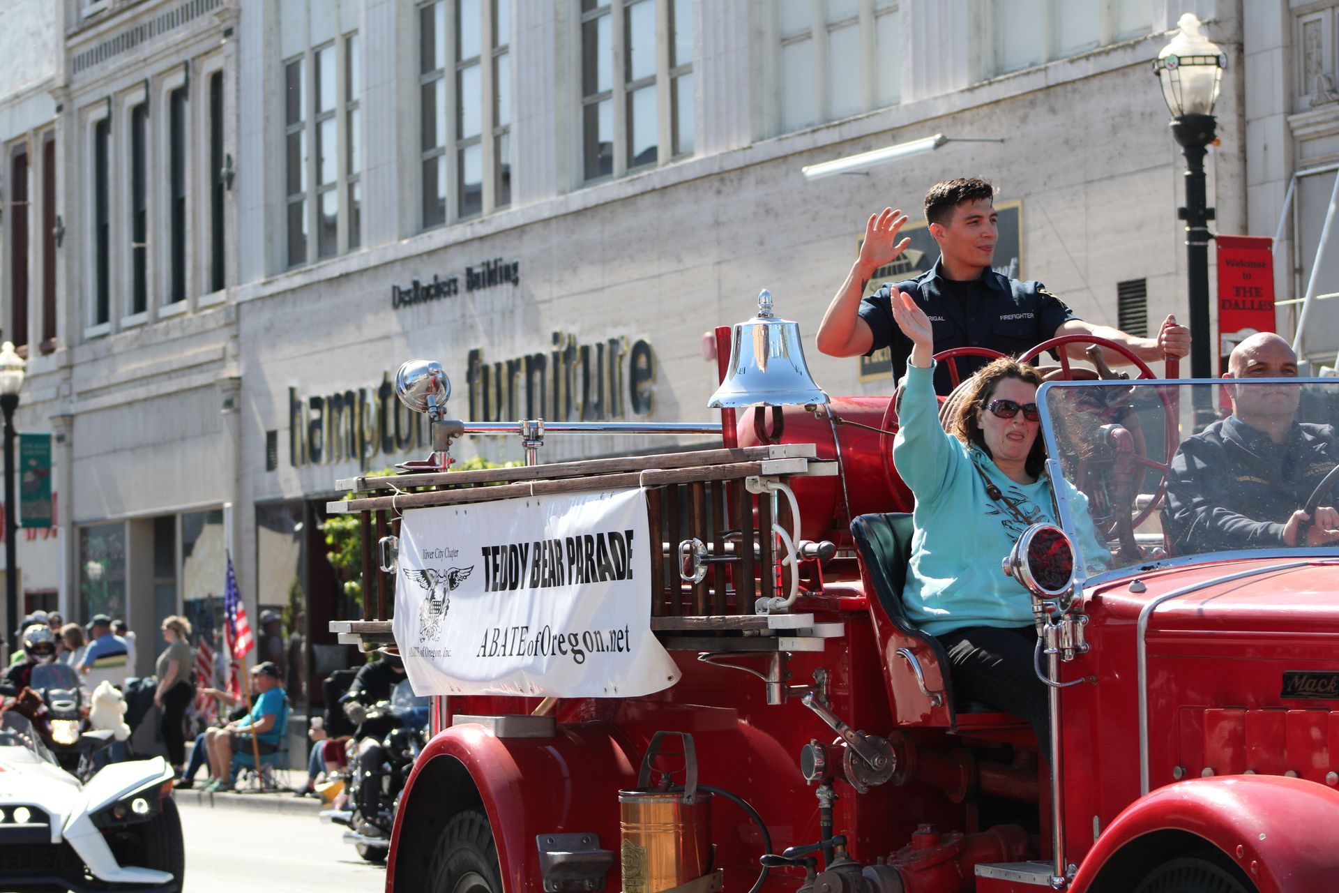 A group of people are riding on the back of a red fire truck in a parade.