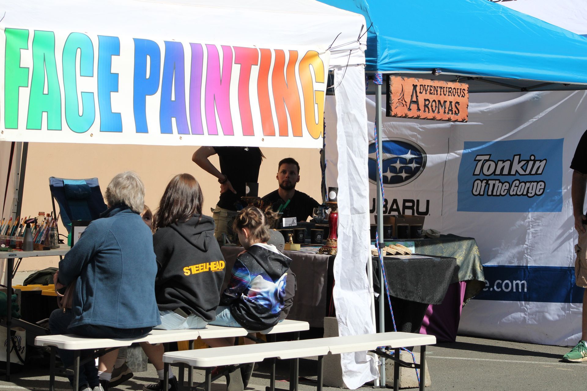 A group of people are sitting under a tent that says face painting