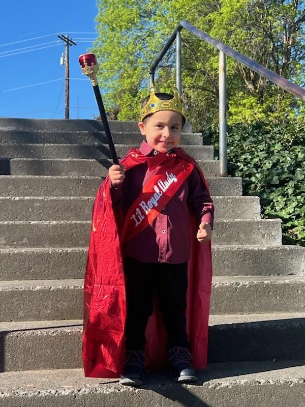 A little boy wearing a crown and cape is standing on stairs