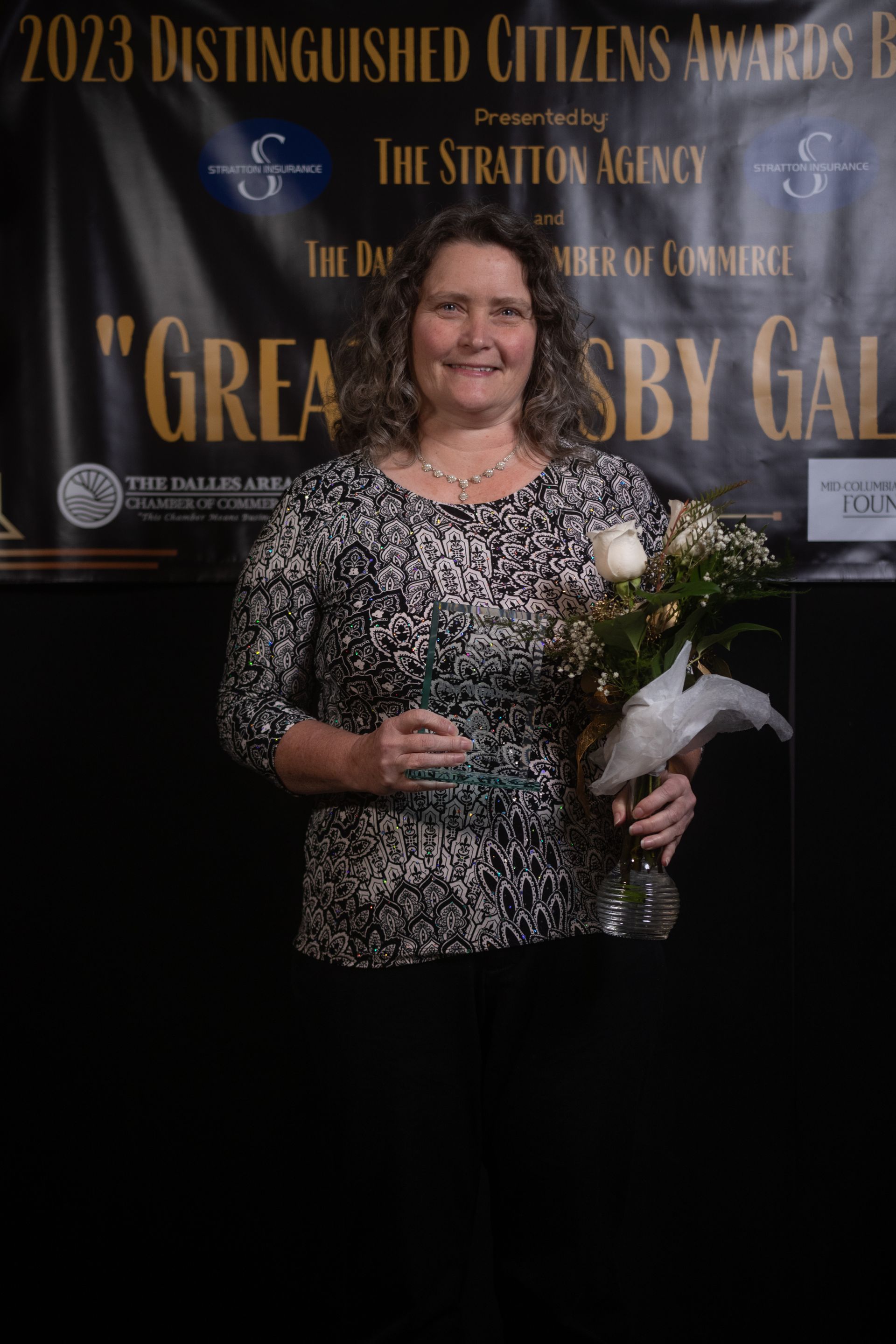A woman is holding a trophy and a bouquet of flowers in front of a sign.