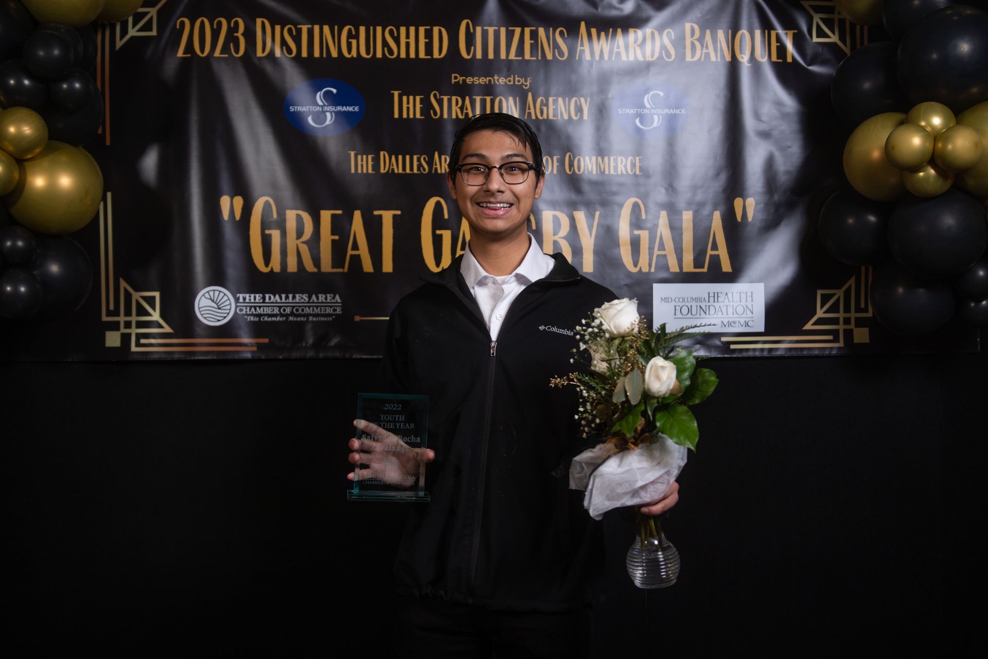 A man is holding a bouquet of flowers in front of a sign that says `` great glory gala ''.