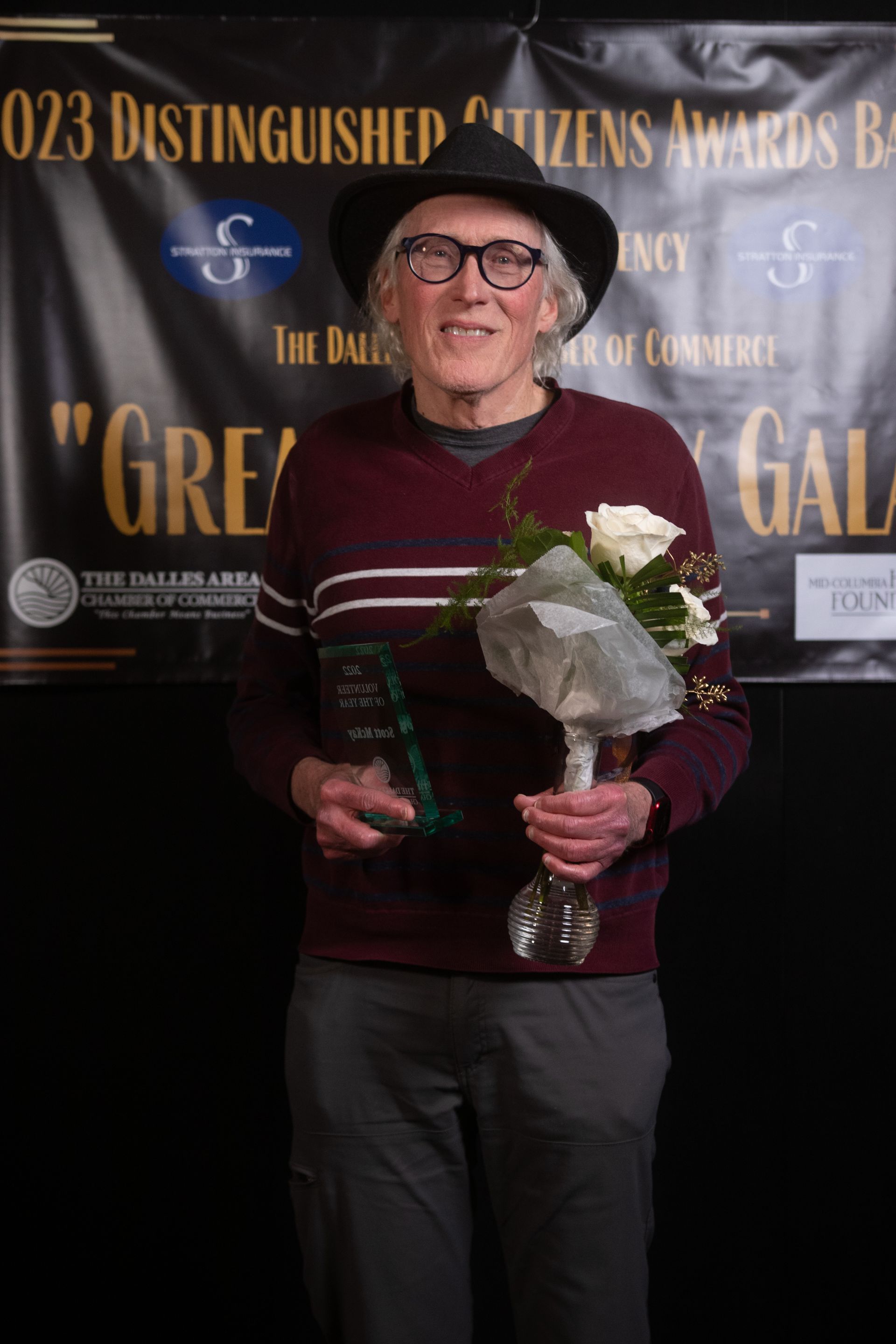 A man in a hat is holding a bouquet of flowers and a trophy.