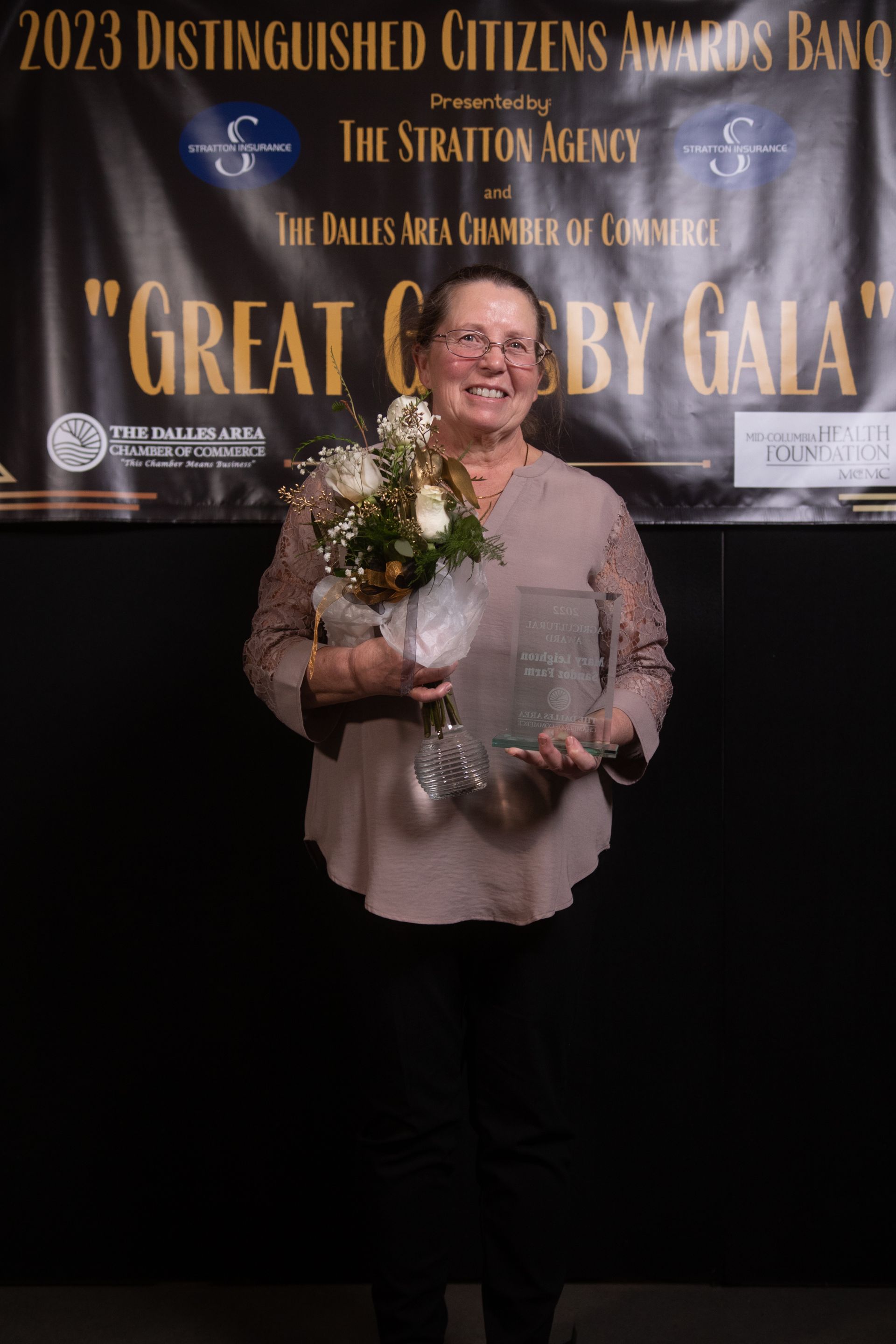 A woman is holding a bouquet of flowers in front of a sign that says great citizens by gala.