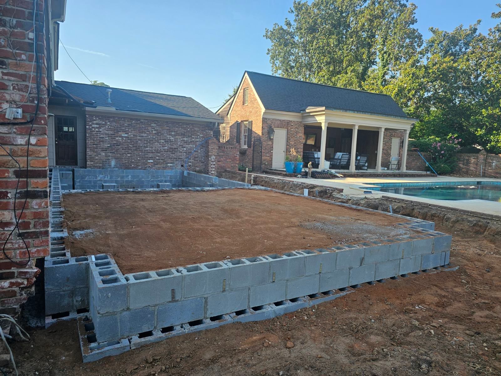 Backyard construction with a concrete block foundation beside a pool and brick house