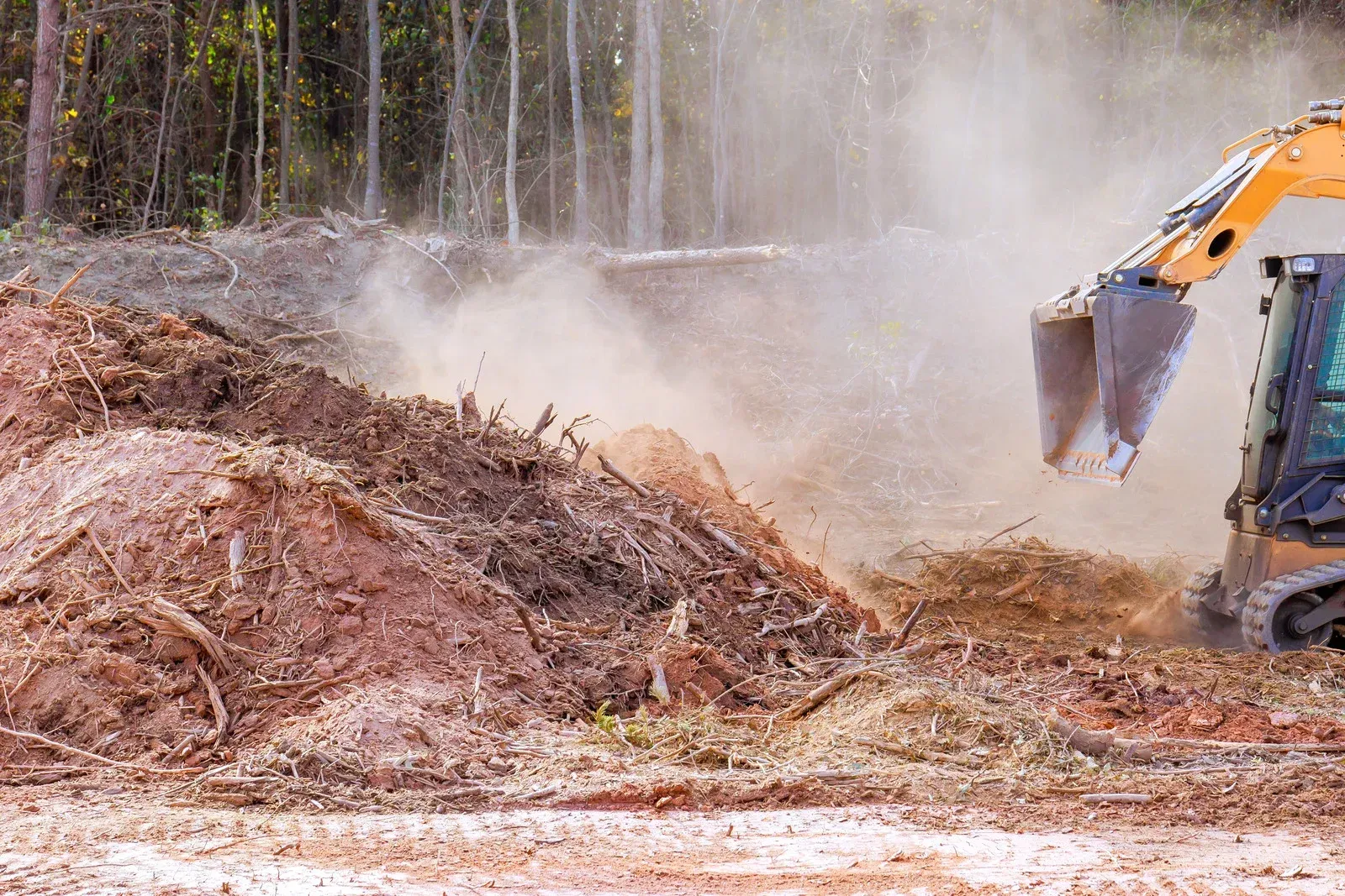 Excavator dumping wood chips in a dusty forest clearing