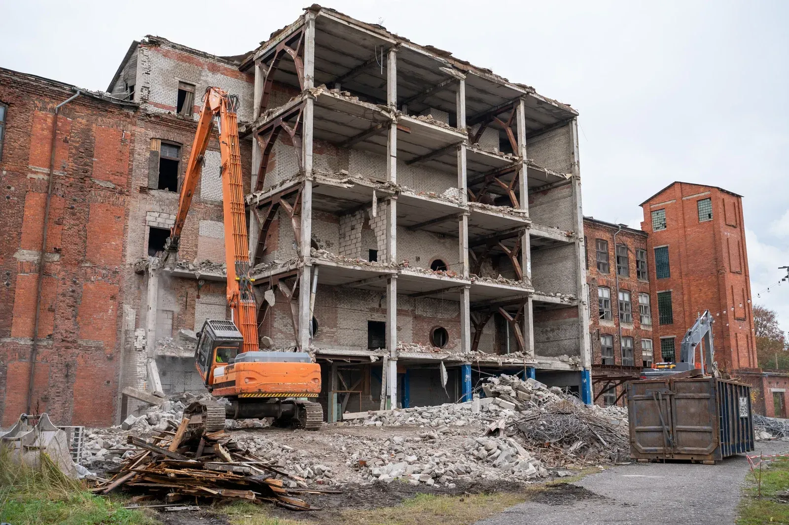 Demolition site with excavator tearing down a concrete building amid rubble and old brick structures