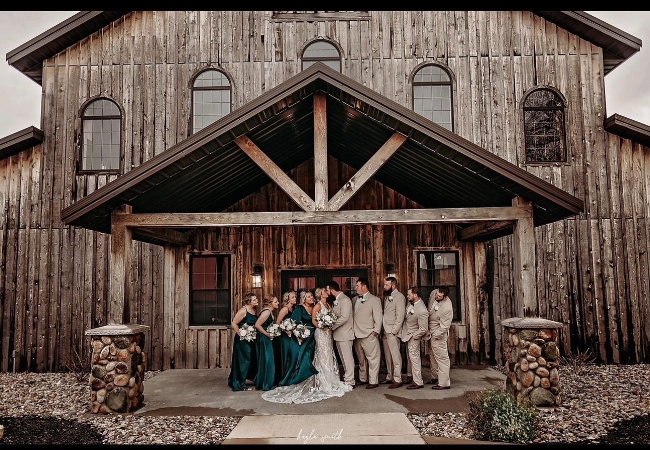 Wedding party posing in front of a rustic wooden barn. Teal and tan attire.
