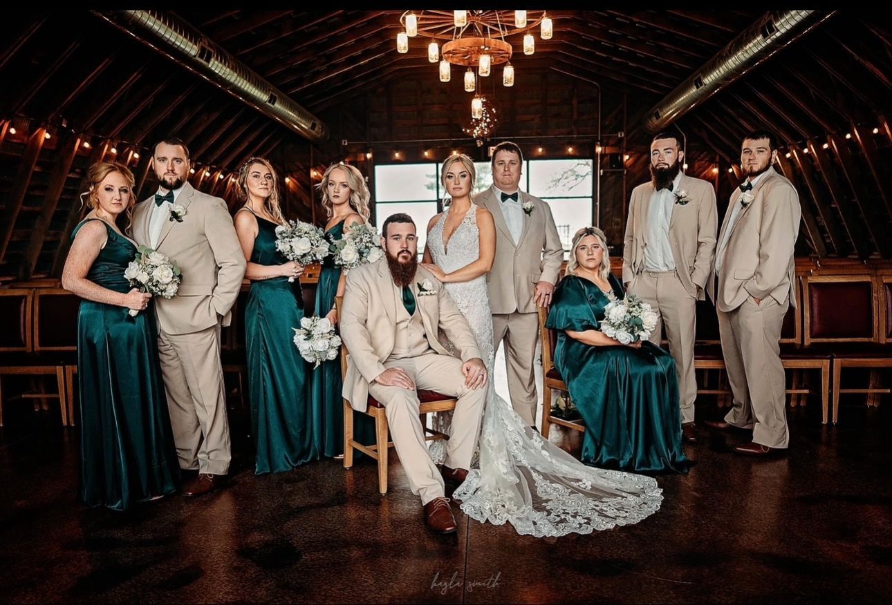 Wedding party poses indoors; bride and groom centered with attendants. Teal dresses, tan suits.