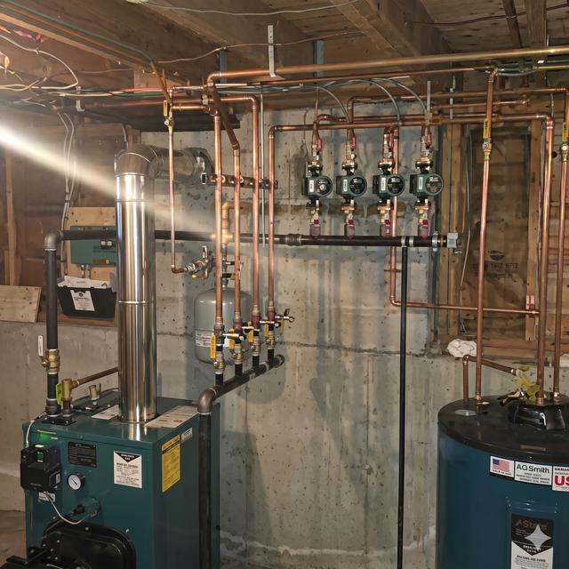 Basement mechanical room with two boilers, copper pipes, and control valves against a concrete wall