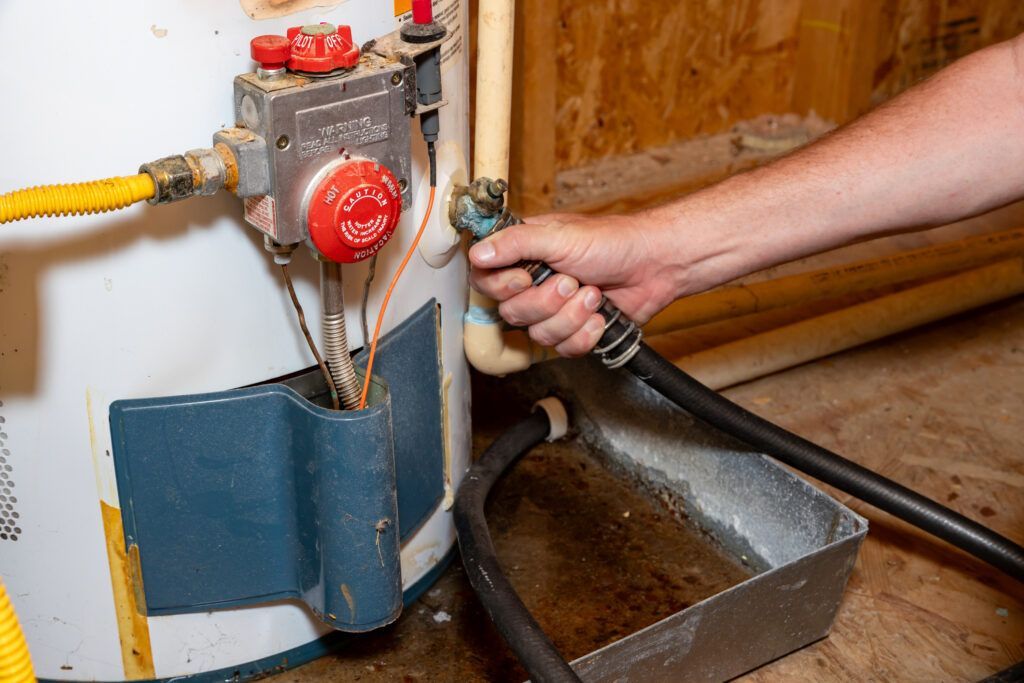 Hand cleaning a boiler pipe with a hose next to a metal drip tray in a kitchen.