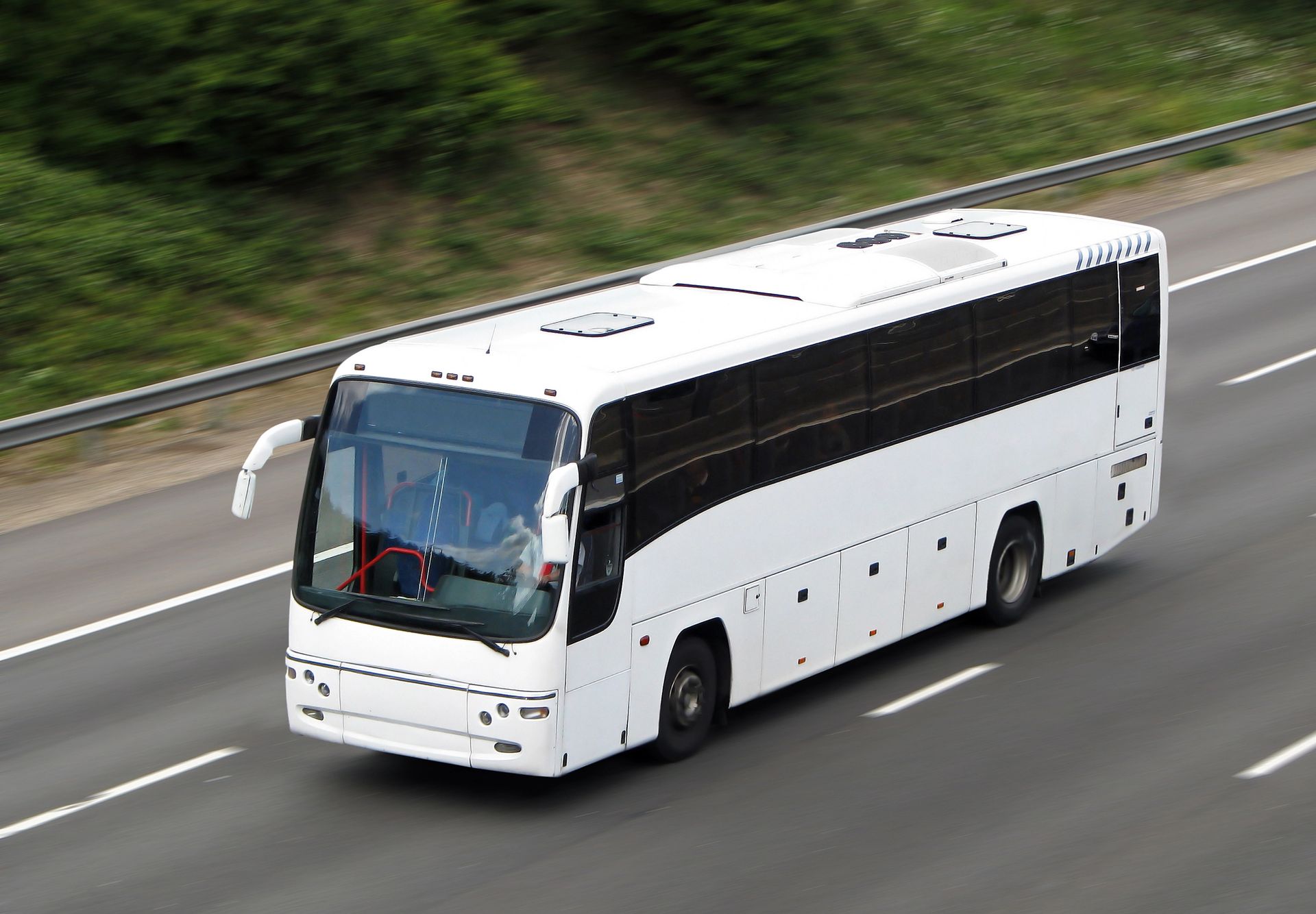 Autobus bianco che viaggia su un'autostrada con fogliame verde sullo sfondo.