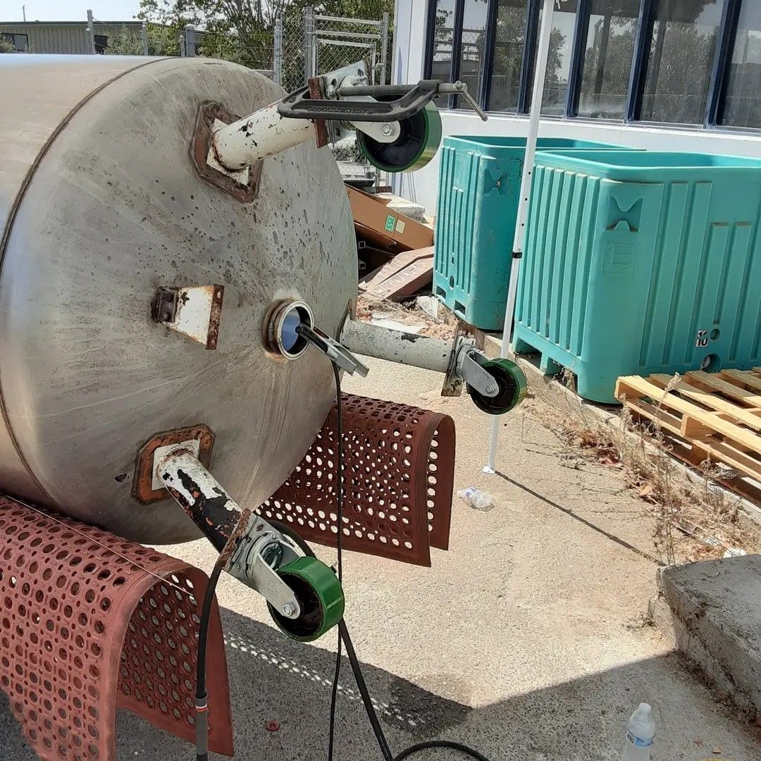 A large stainless steel tank with wheels and a hose attached to it