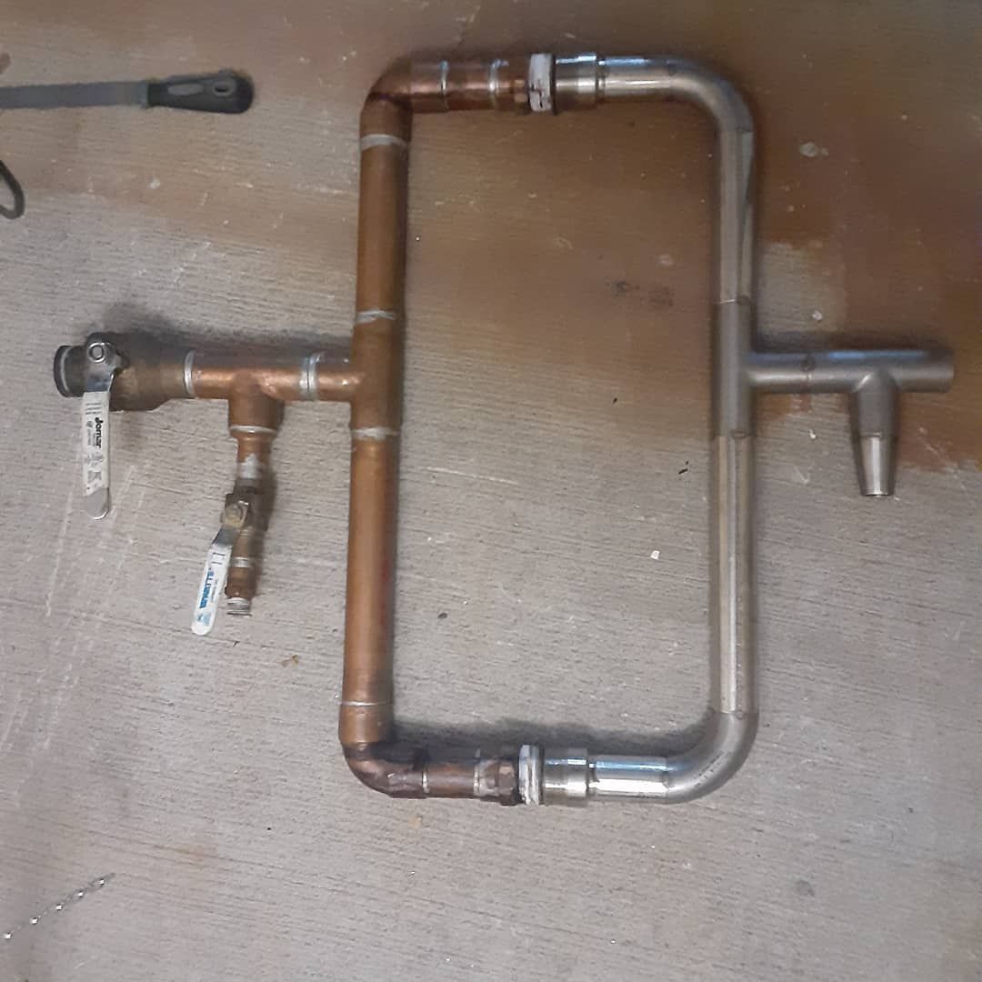 A copper pipe with a valve attached to it is sitting on the floor.