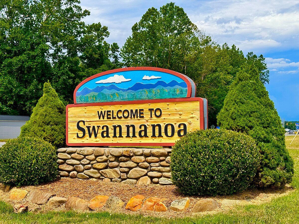 A welcome to swannanoa sign is surrounded by bushes and rocks.