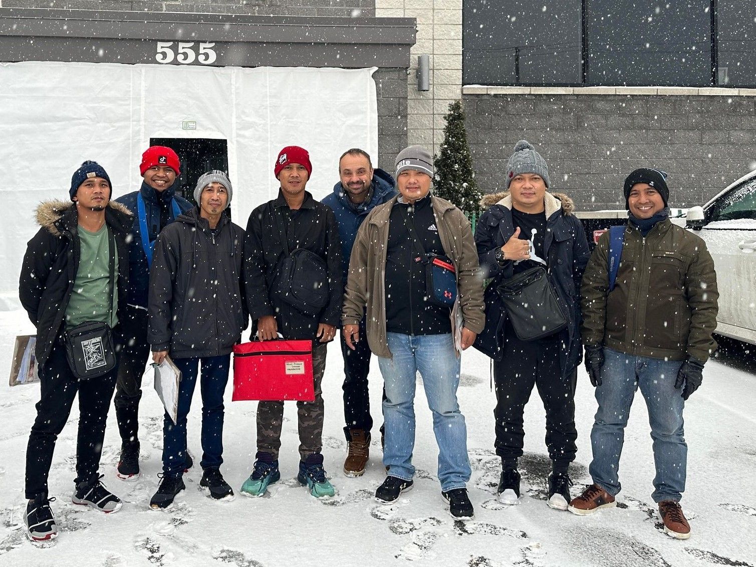 A group of men are standing in the snow in front of a building.