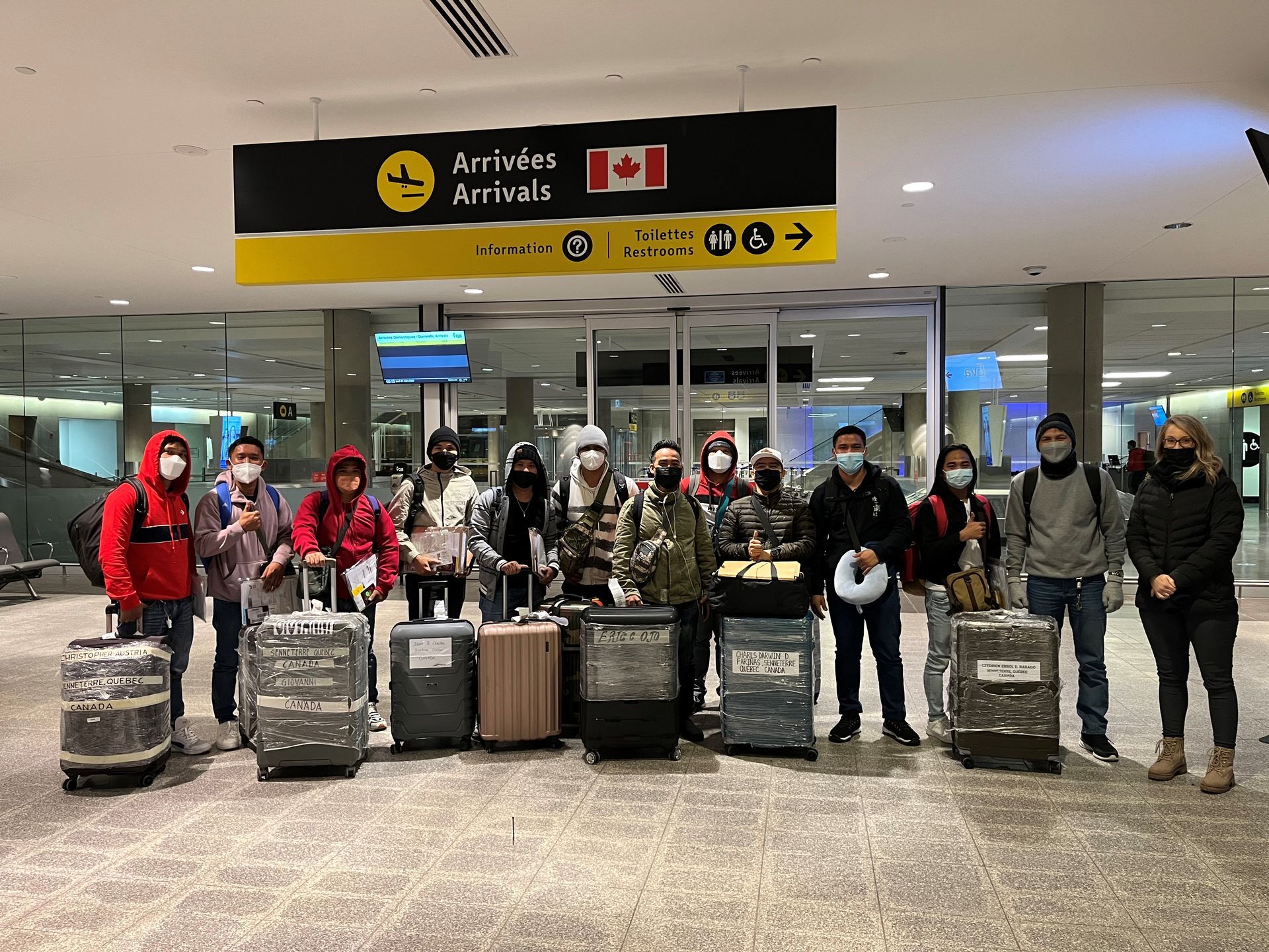 A group of people wearing masks are standing in front of luggage at an airport.