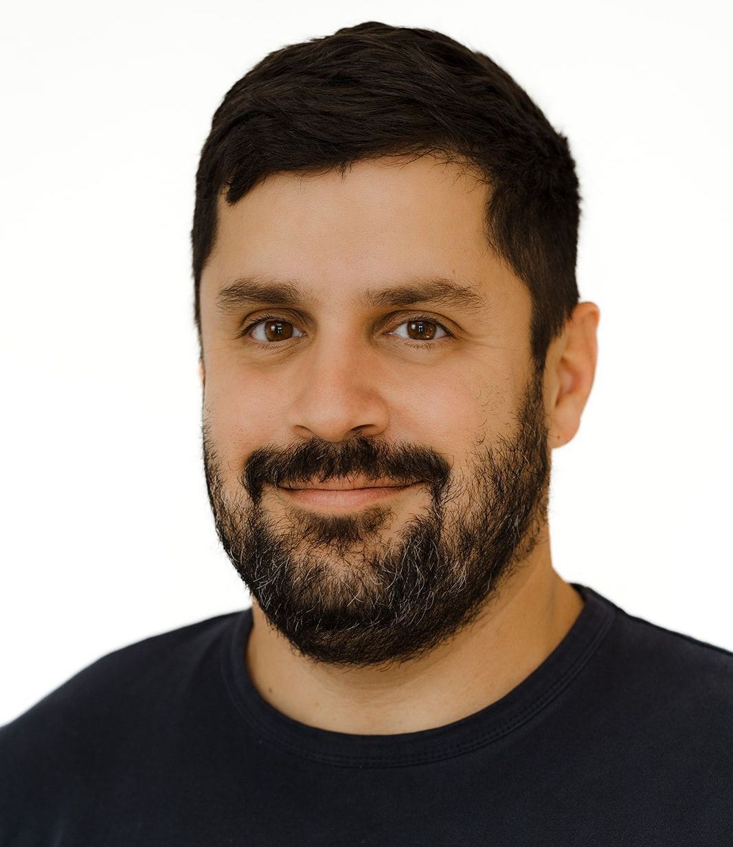 A man with a beard is wearing a black shirt and smiling.