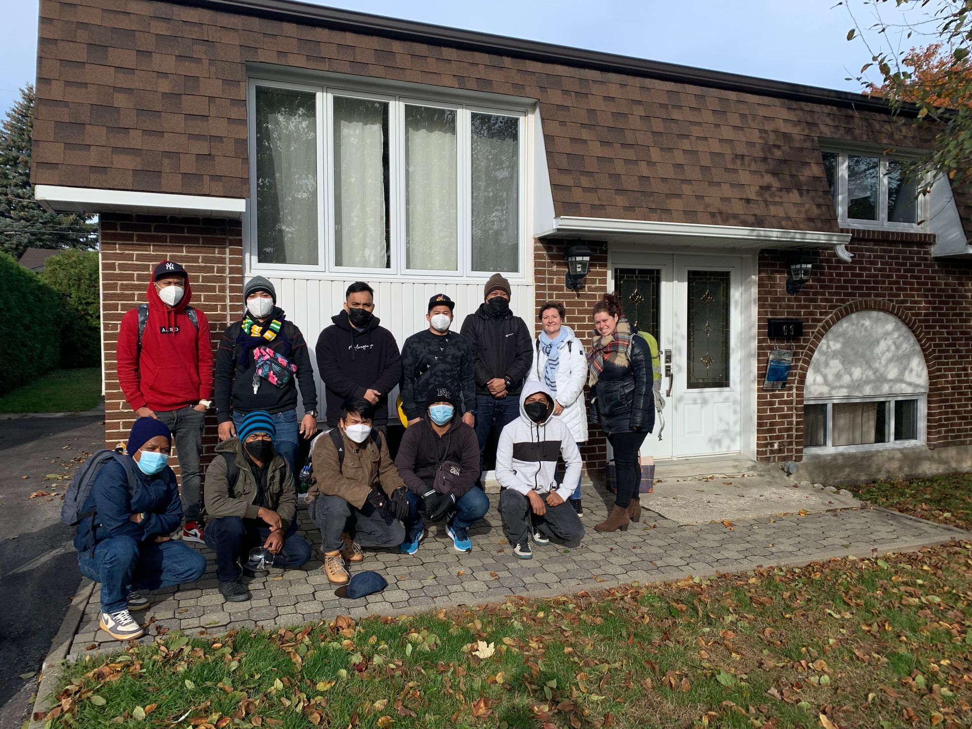 A group of people wearing masks are posing for a picture in front of a house.