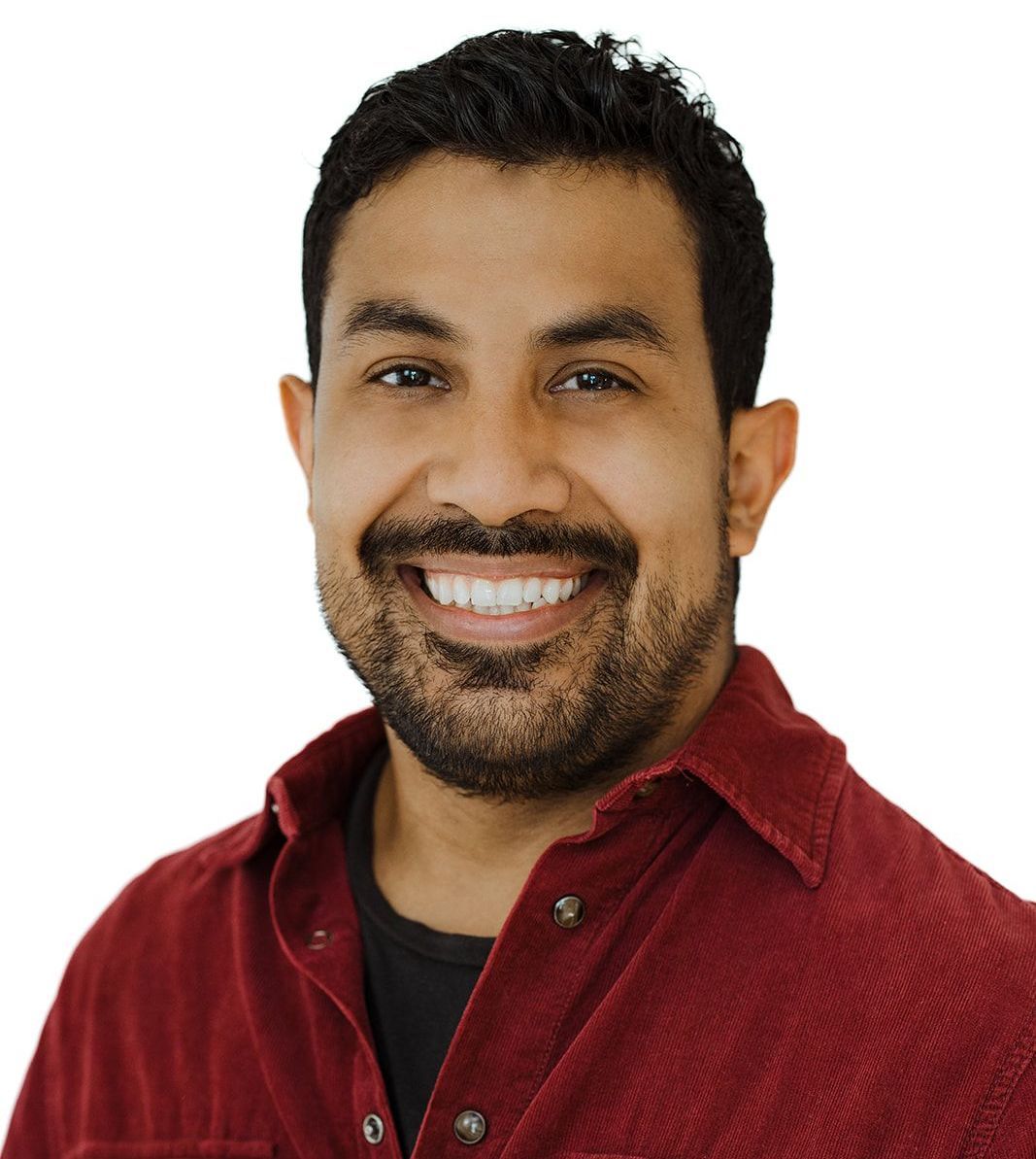 A man with a beard is wearing a red shirt and smiling
