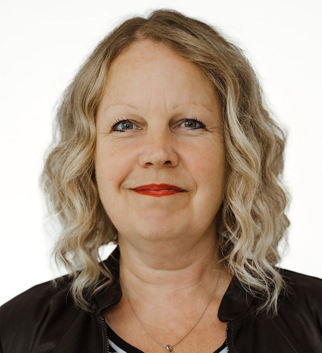A woman with blonde hair and red lips is wearing a black jacket and necklace.