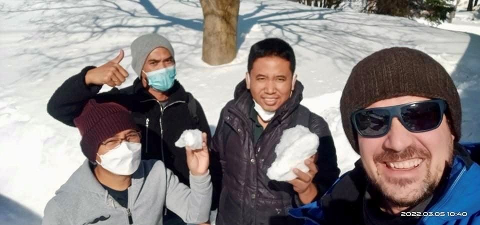 A group of men wearing face masks and sunglasses are standing in the snow.
