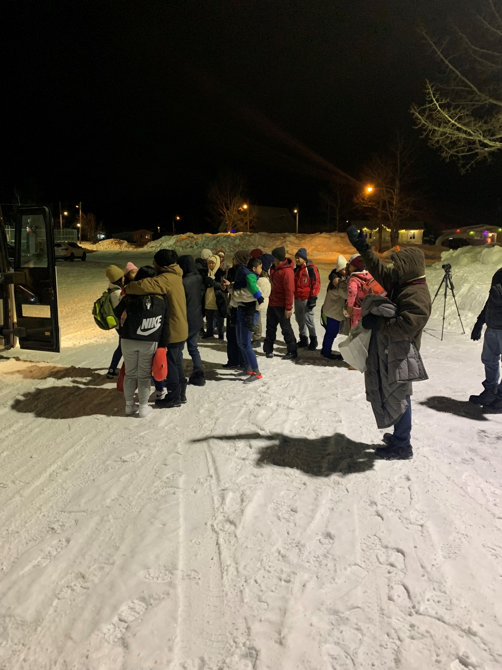 A group of people are standing in the snow at night.
