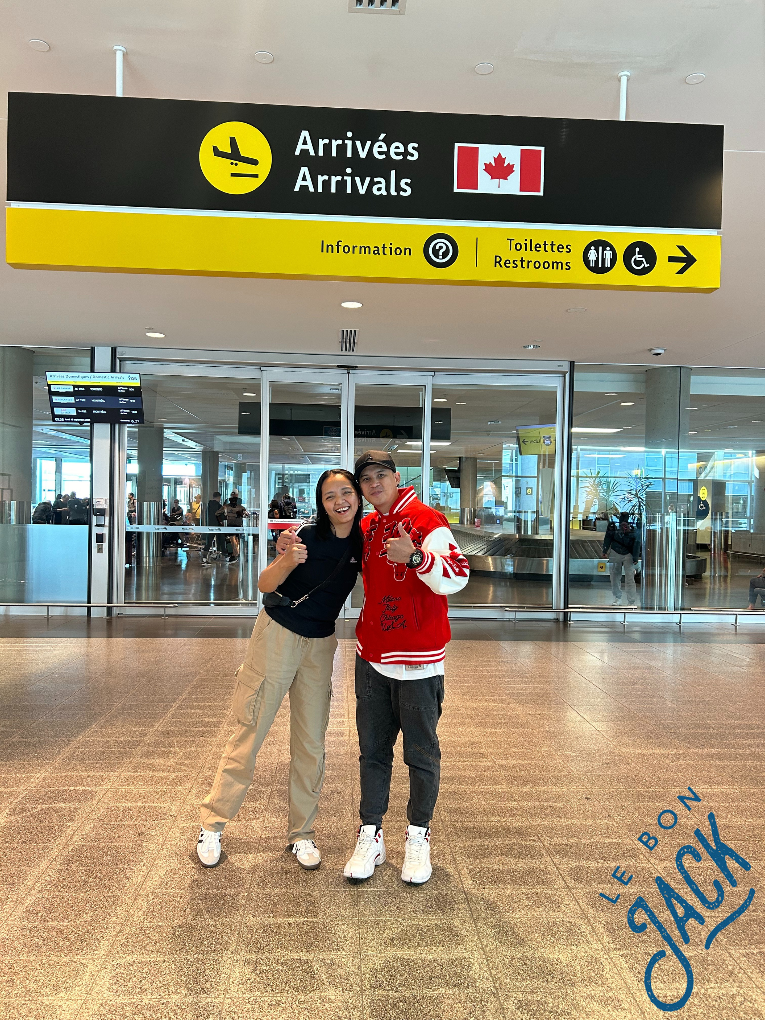 A man and a woman are posing for a picture in front of a sign that says arrivées arrivals
