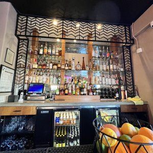 A bar with a lot of bottles and a basket of fruit on the counter.