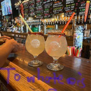 Two glasses of drinks are sitting on a wooden bar.