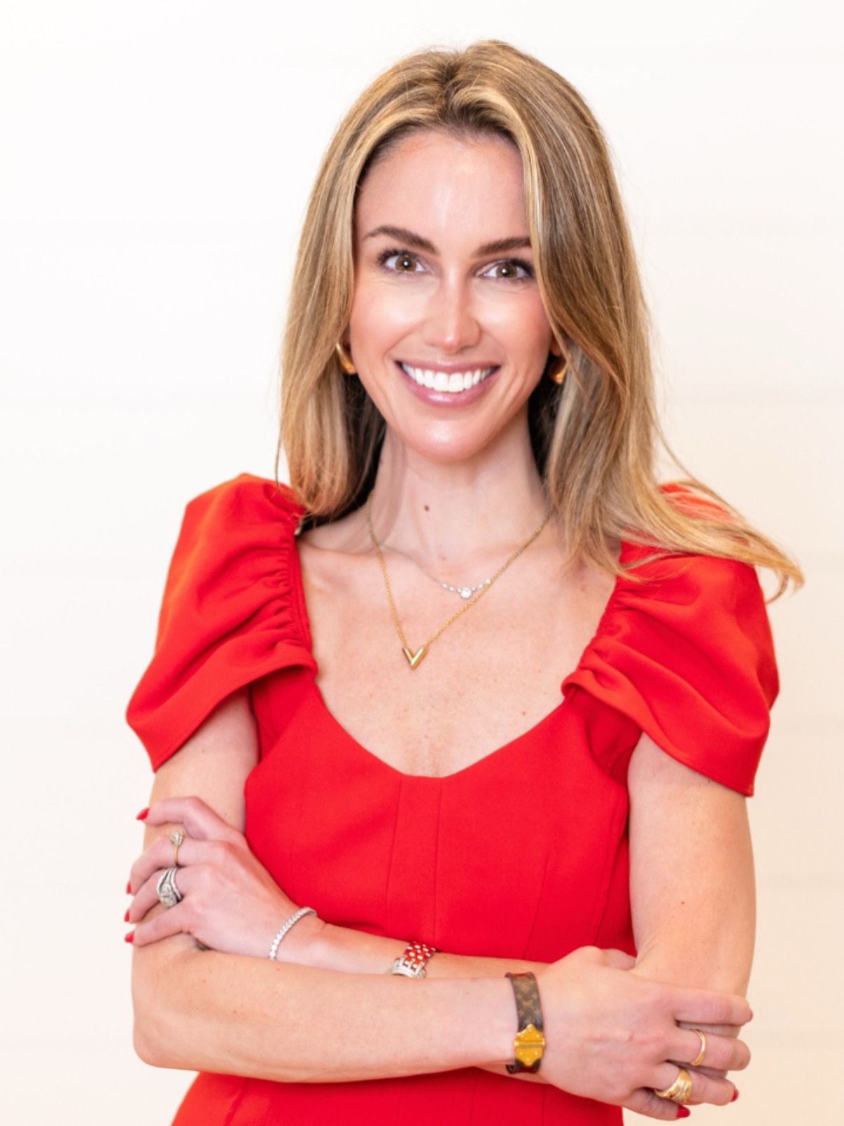 Ashley Cashon headshot smiling in a red dress with arms crossed, white background, featured on About Me page