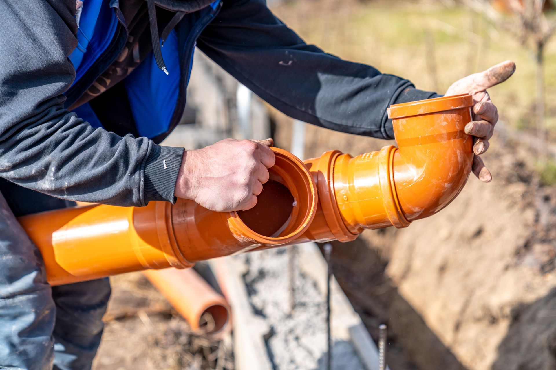 Technician connecting underground plastic drain pipes during sewer line services.