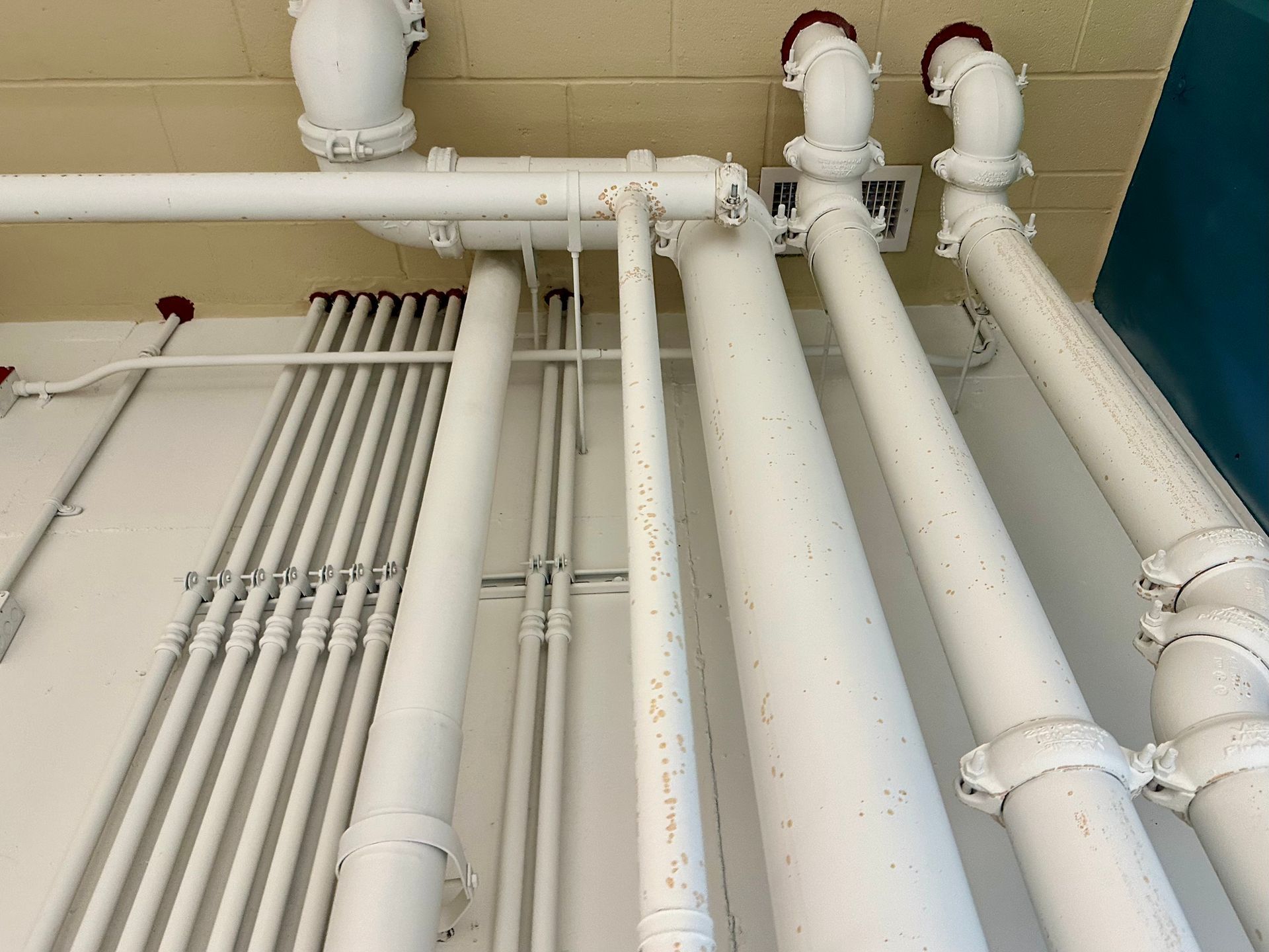 White pipes and conduits run along a white wall and ceiling in a building.