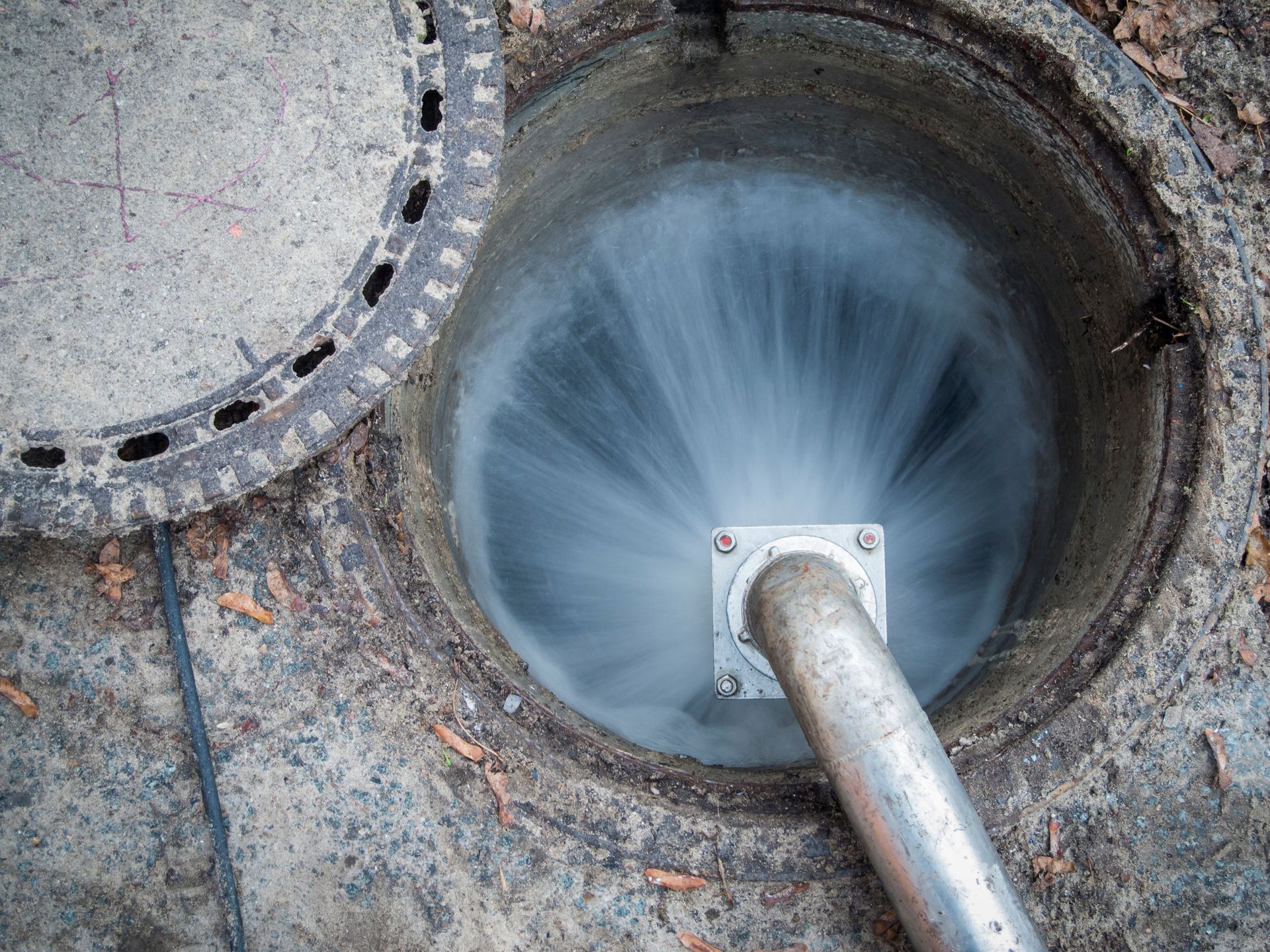 Water spraying forcefully from pipe in open manhole.