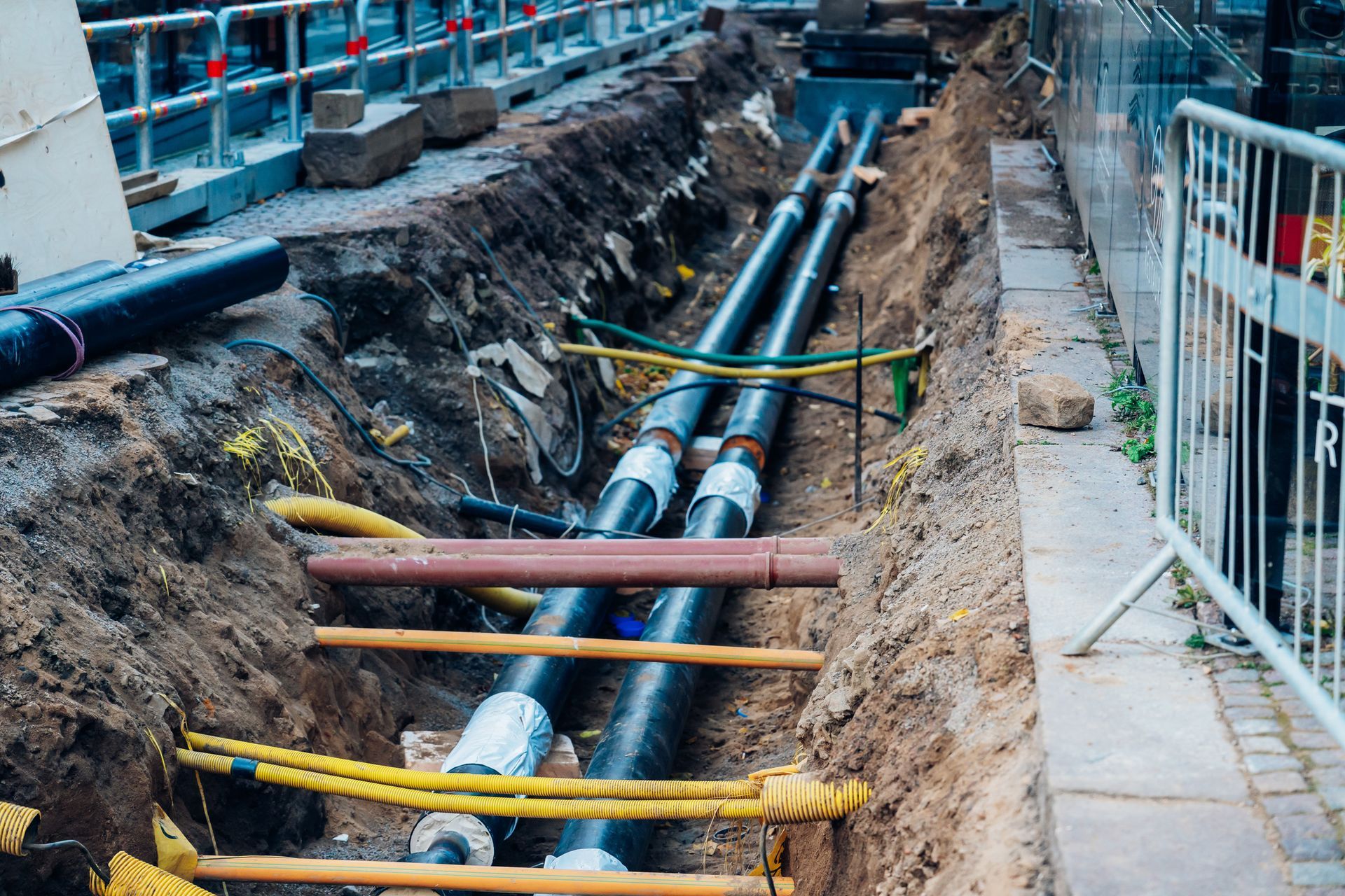 Trench with two black pipes and yellow cables laid for construction.