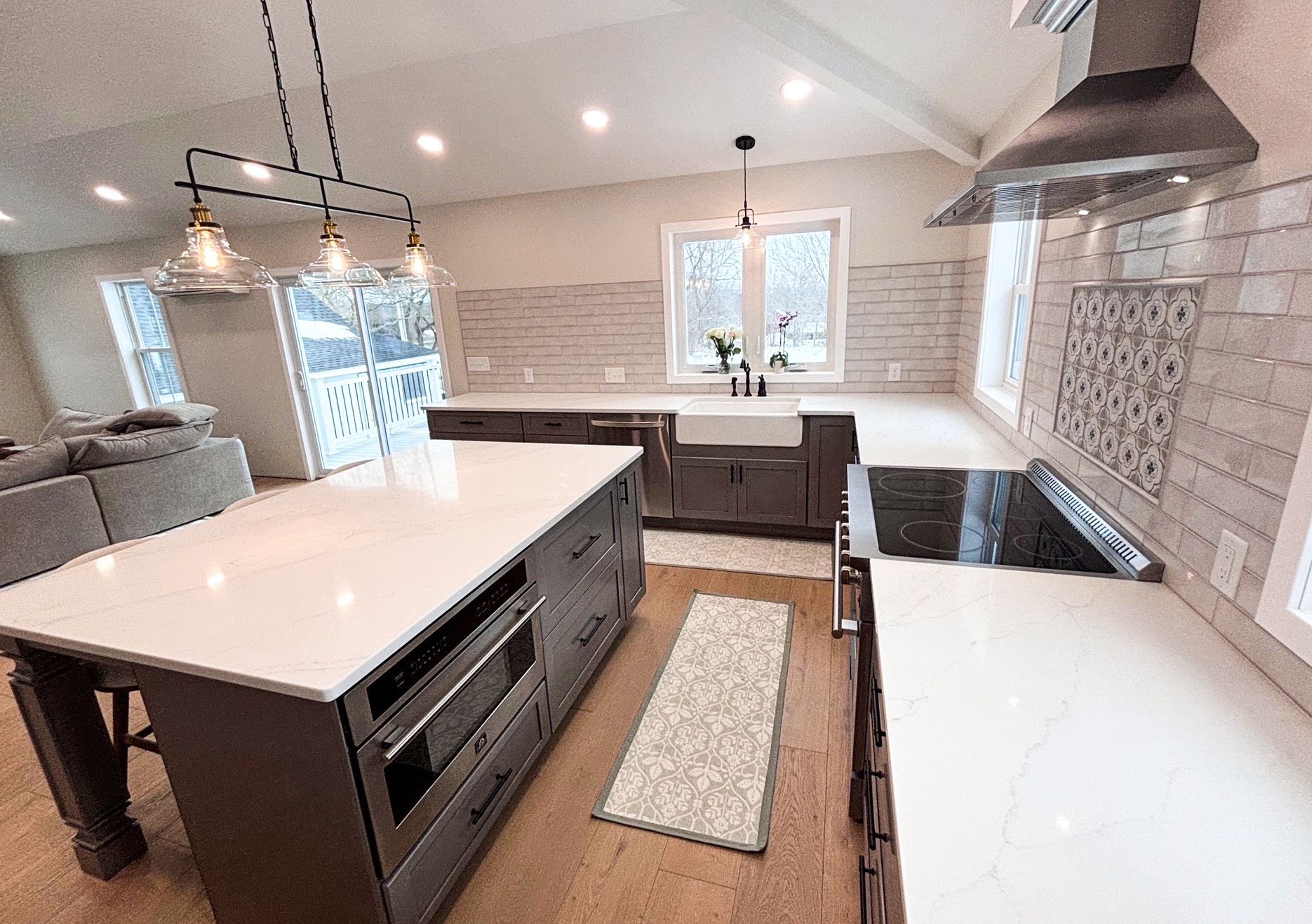 Bright modern kitchen with white island, wood floors, large window, and stainless steel range hood.