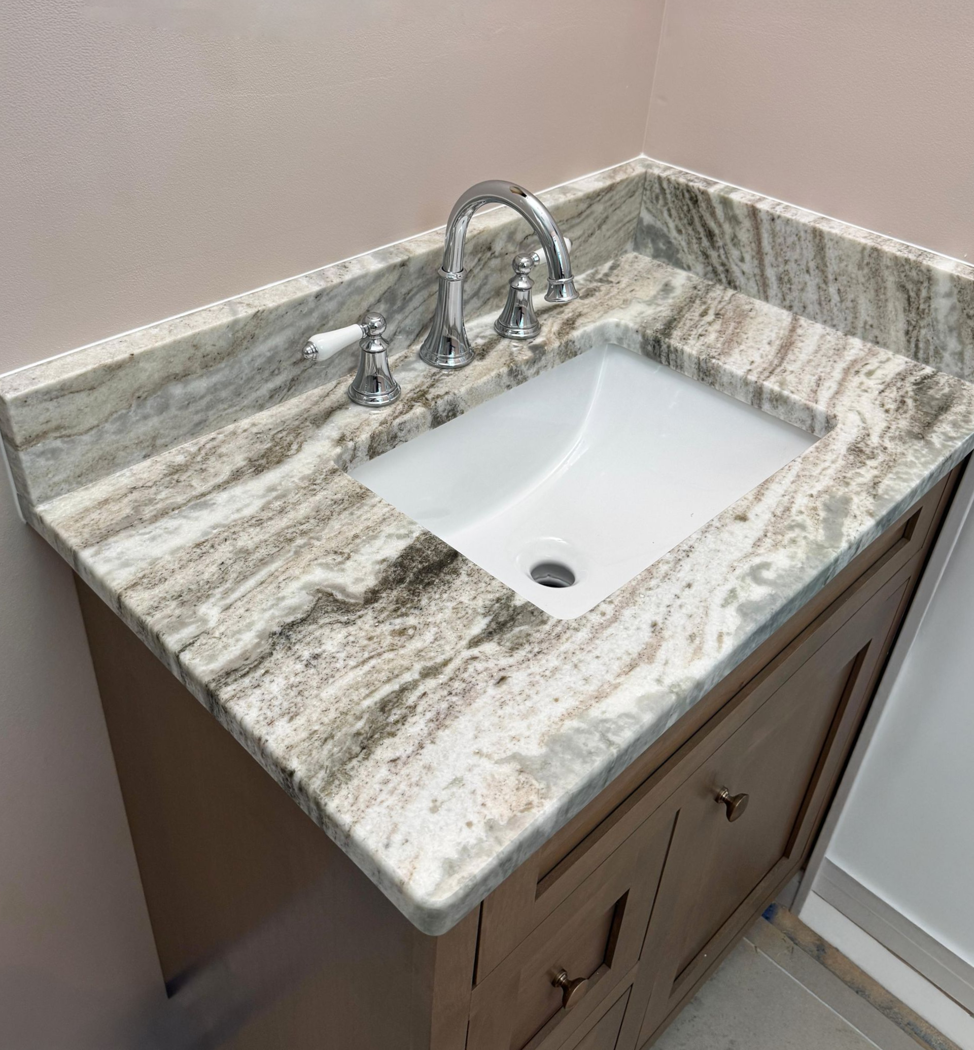 Corner bathroom vanity with granite countertop and white sink against a beige wall