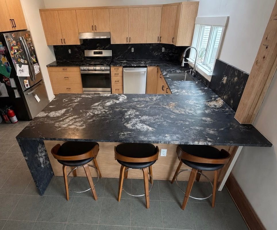 Modern kitchen with black marble island, wood cabinets, and three stools by a window.