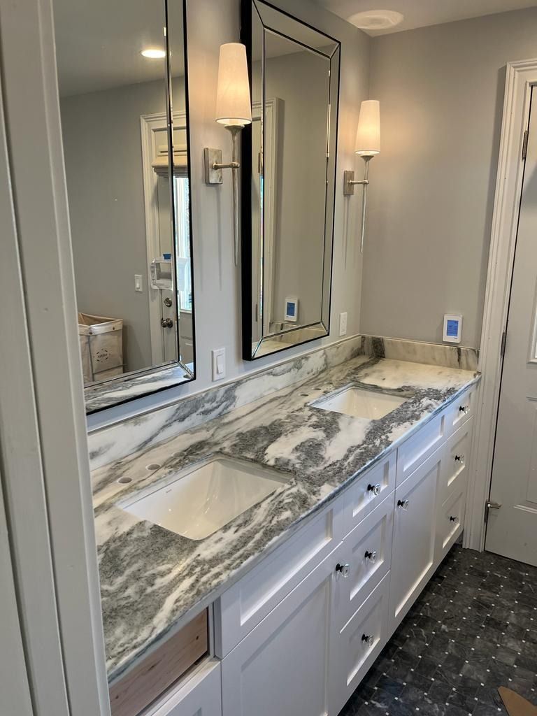 Bathroom vanity with marble countertop, mirrored cabinets, and wall sconces beside a shower door