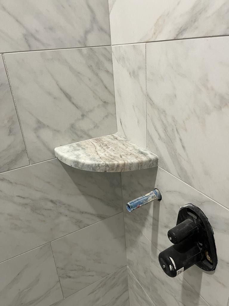Corner shower shelf with marble-look tile and a black shower valve knob