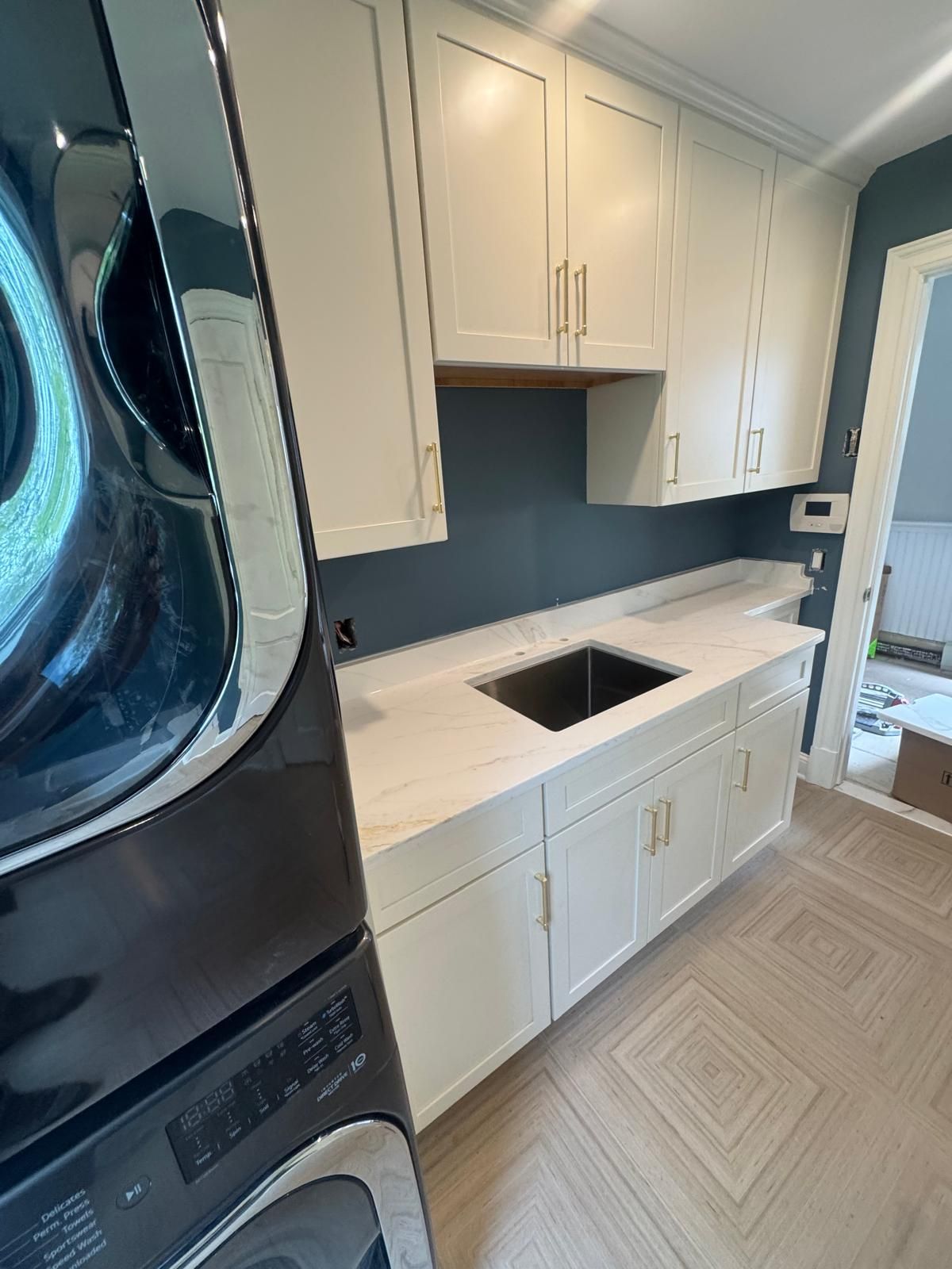 Compact laundry room with white cabinets, dark countertop, sink cutout, and stacked washer-dryer by a window.