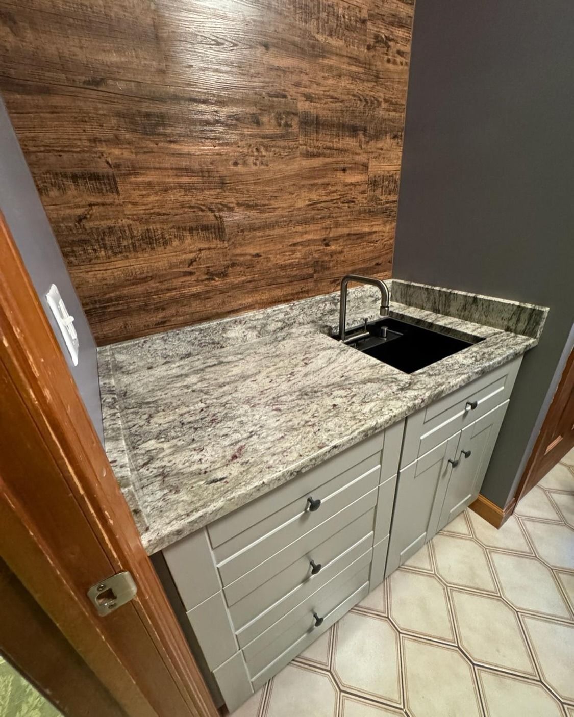 Granite countertop with sink and light gray cabinets in a small room with wood accent wall