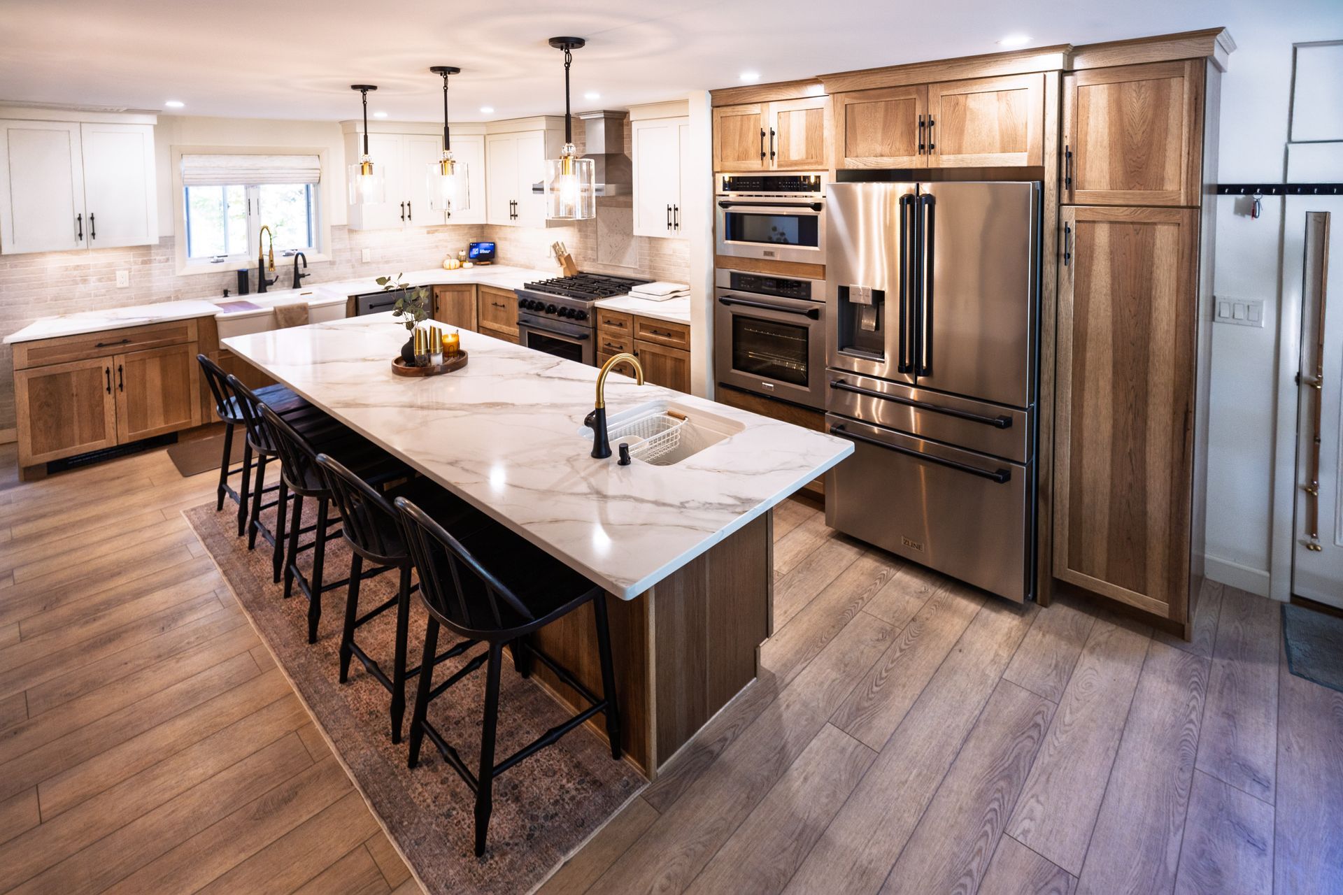 Modern kitchen with large island, marble countertop, black stools, stainless steel appliances, and wood cabinetry