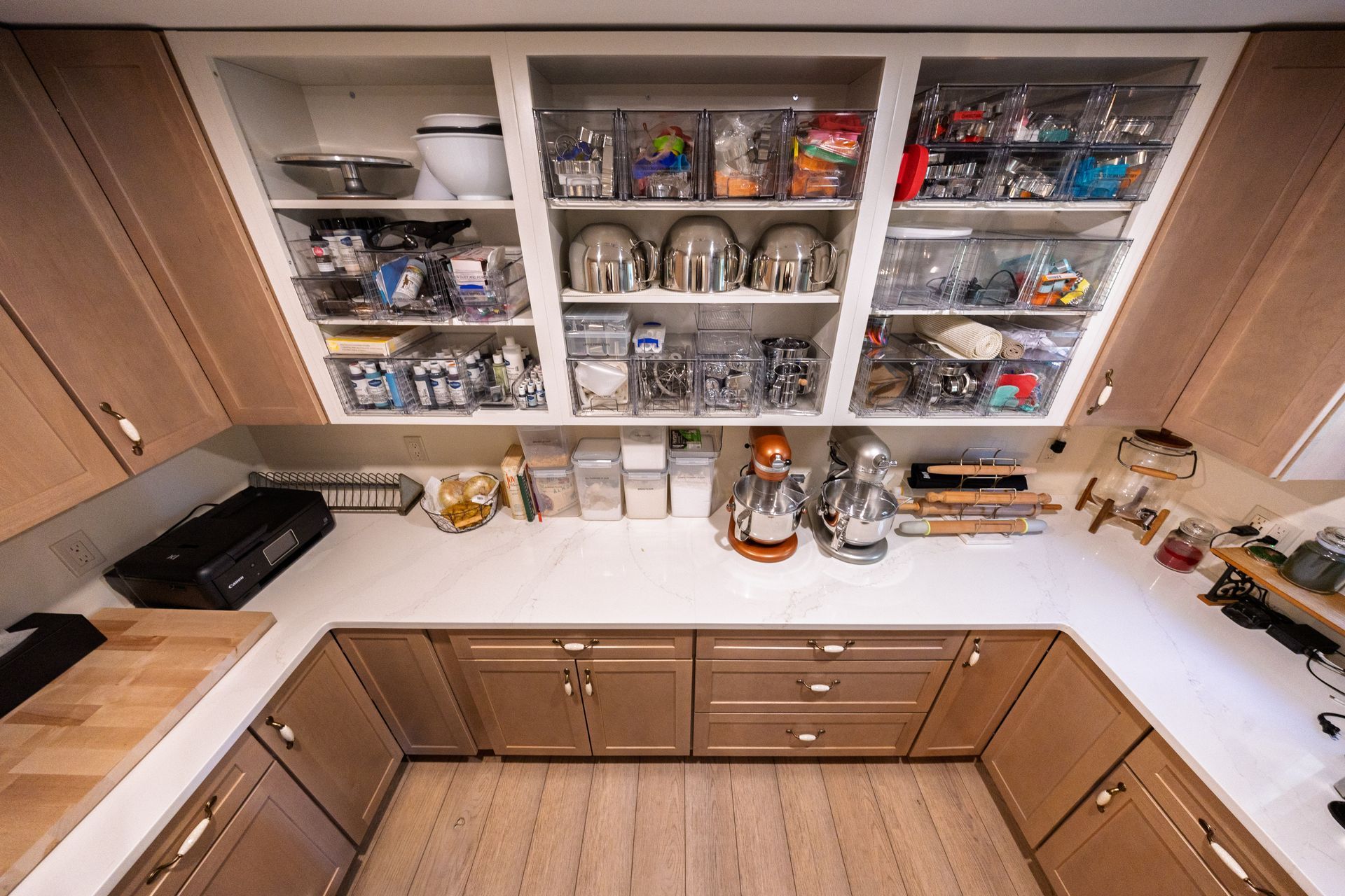 Kitchen pantry shelves with jars and containers above a white countertop and wooden cabinets.