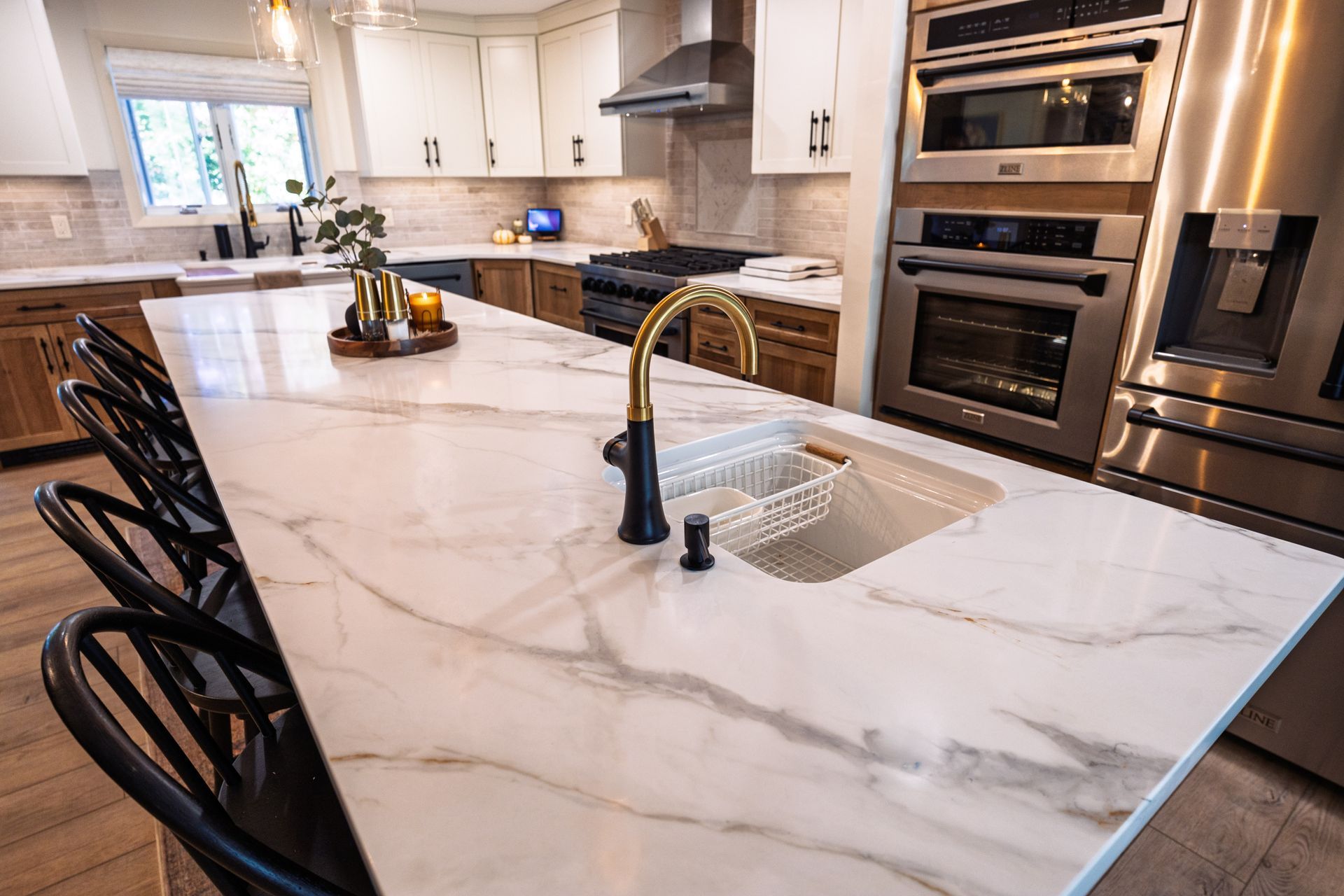 Modern kitchen with white marble island, black barstools, farmhouse sink, and built-in stainless appliances