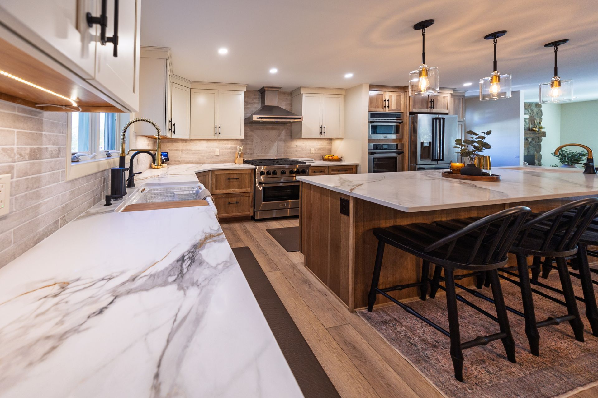 Bright modern kitchen with white marble counters, wood island, bar stools, and stainless steel appliances