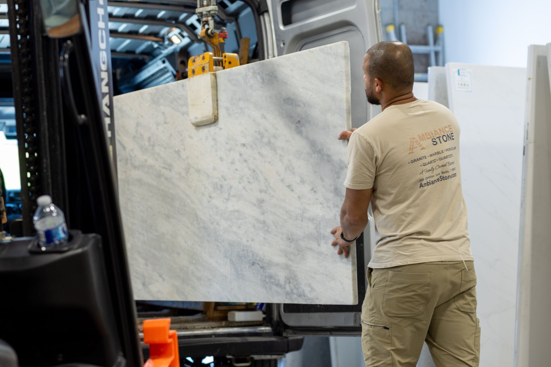 Worker moving a large marble slab beside industrial machinery in a workshop