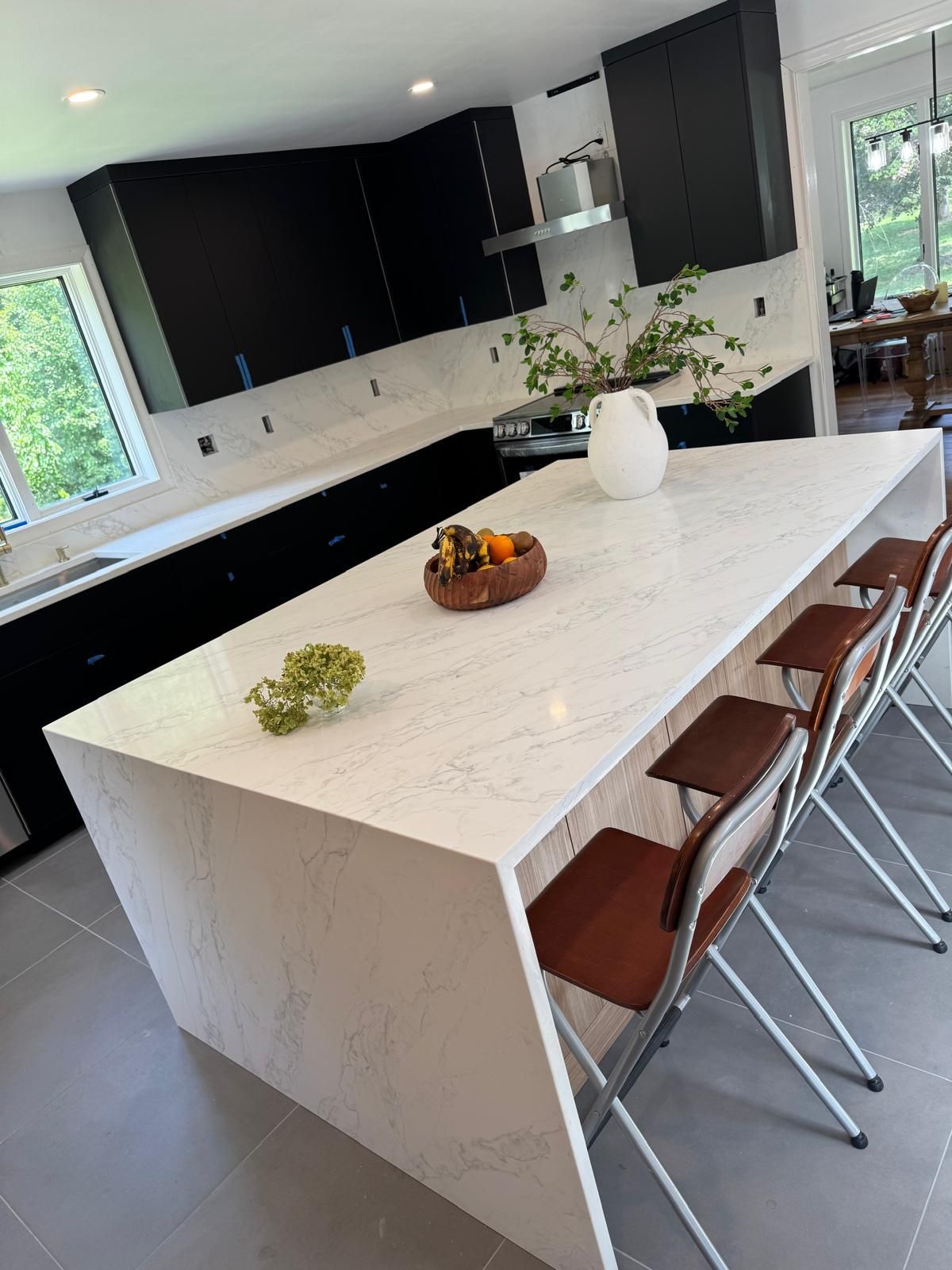 Modern kitchen with a large white island, black cabinets, and bar stools by a window