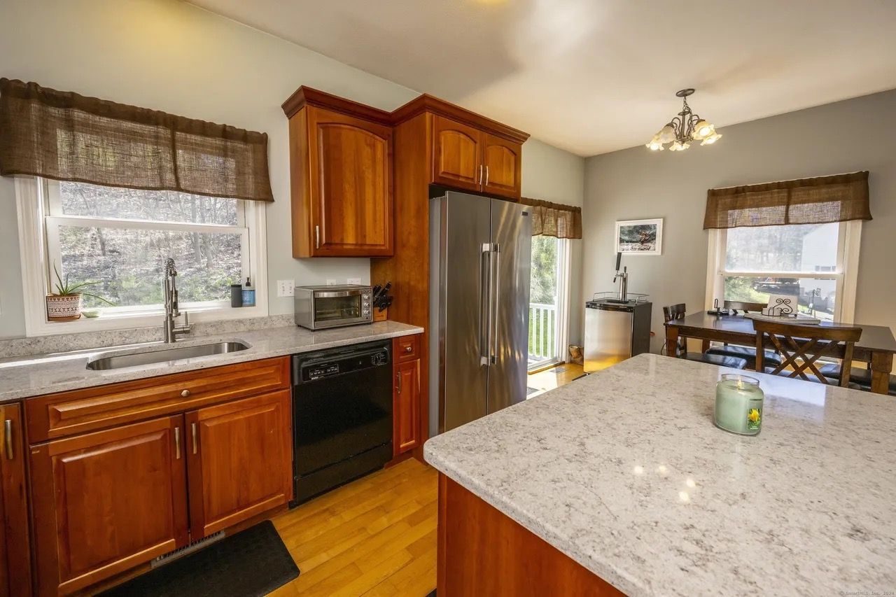 Bright kitchen with wood cabinets, stainless fridge, granite island, and dining table by windows