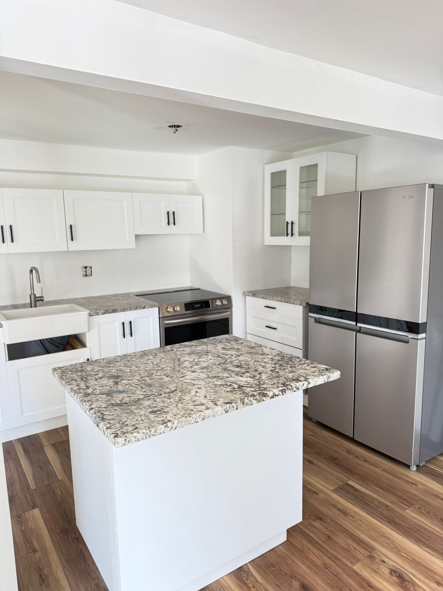 Modern white kitchen with granite island, stainless steel fridge, and wood flooring